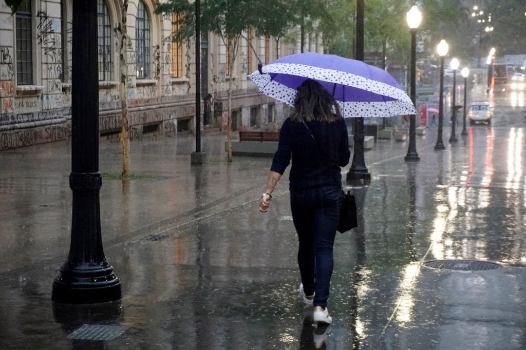 Woman with umbrellas walking on a street in São Paulo while it rains