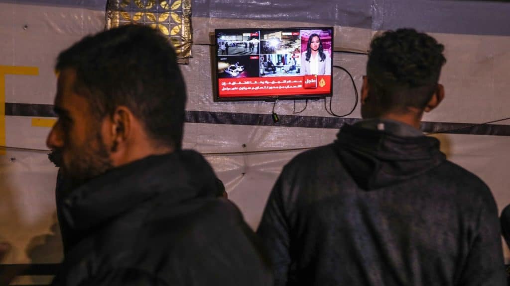 Photo with television with the background and a man with his back watching news about leaving the fire between Israel and Hamas, and another man goes there.