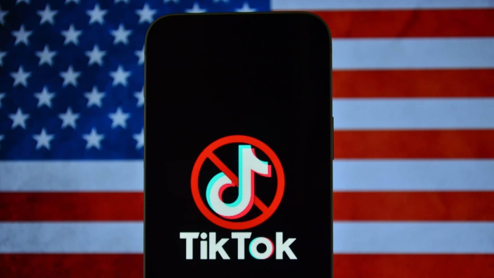 TikTok logo with a ban icon on top of it on a smartphone; behind, the flag of the United States